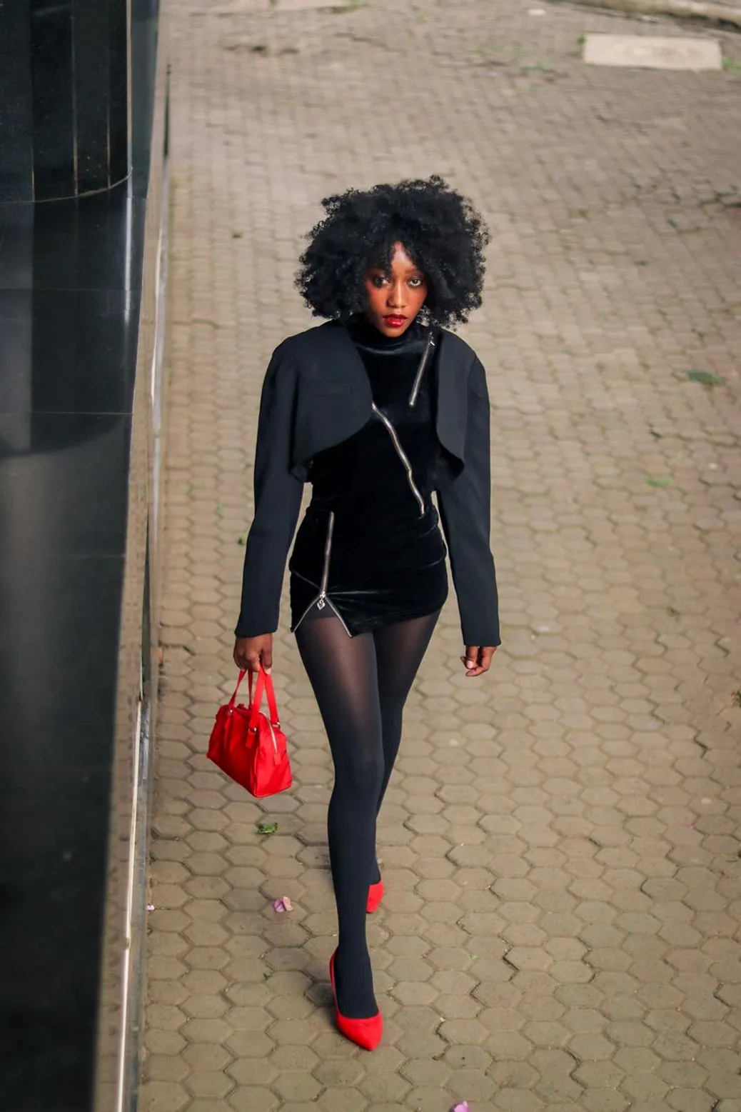 A fashionable woman in an all-black outfit with red accessories walking confidently.