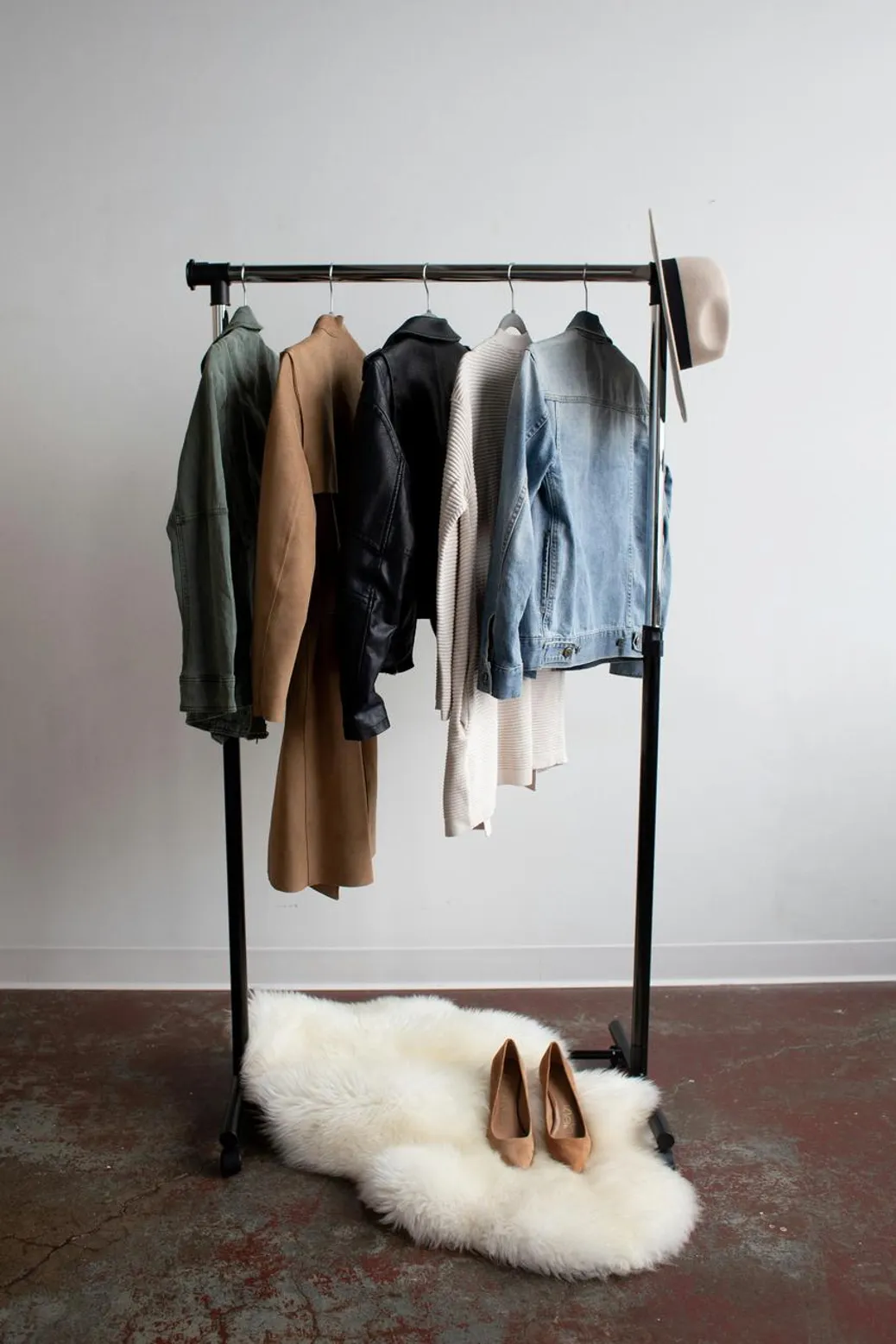A minimalist clothing，stylish jackets， a beige hat, and suede heels，placed on a white fur rug
