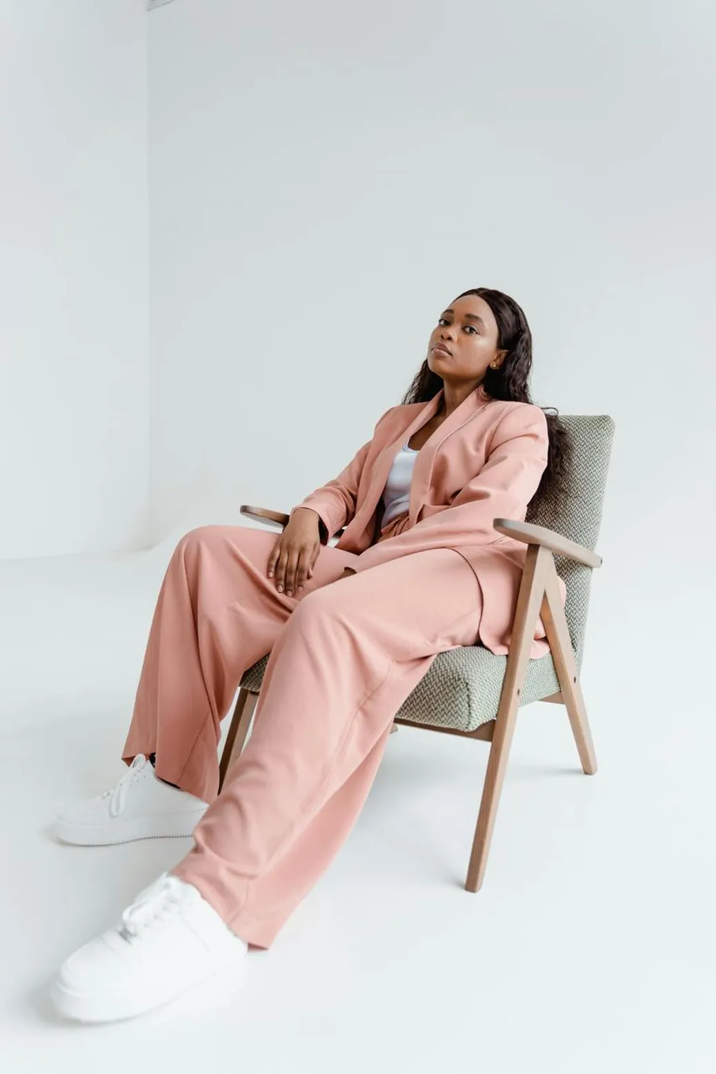 A confident woman in a pastel pink suit lounging in a stylish chair.