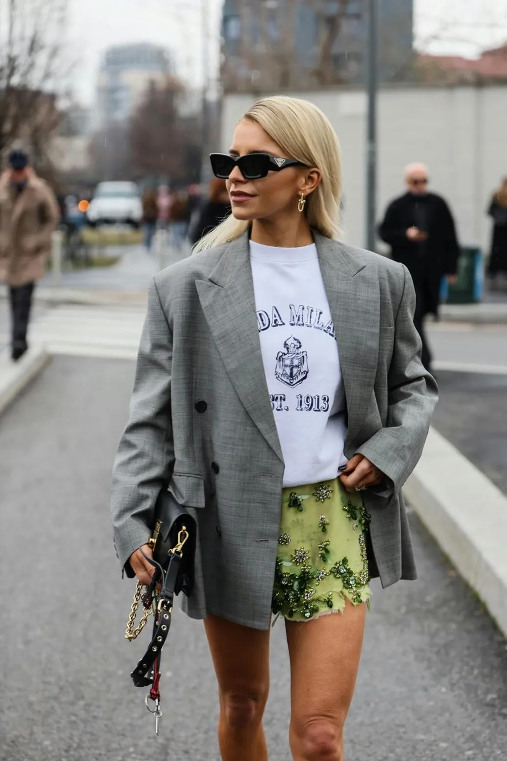 A stylish woman in an oversized blazer, graphic tee, and embellished skirt walking through the city.