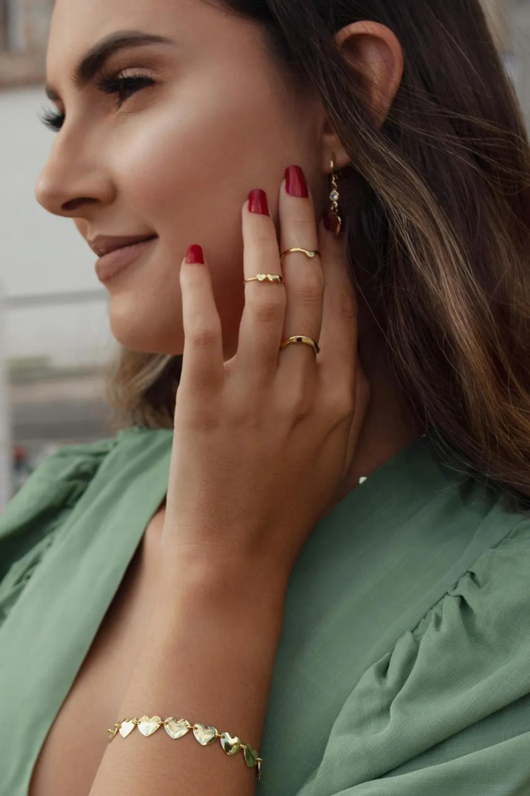 Close-up of a woman’s hand wearing elegant gold rings and a heart bracelet